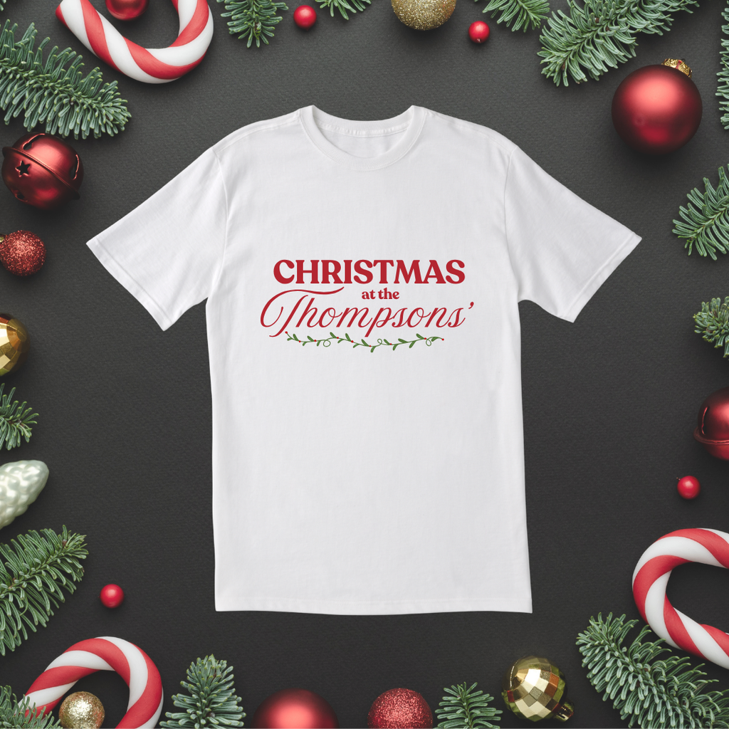 Woman wearing a white “Christmas at the Thompsons’” T-shirt in front of a Christmas tree and wreath.